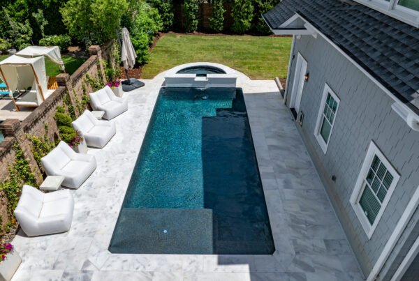 In-ground plunge pool in a backyard next to a garage with outdoor sofas on the left